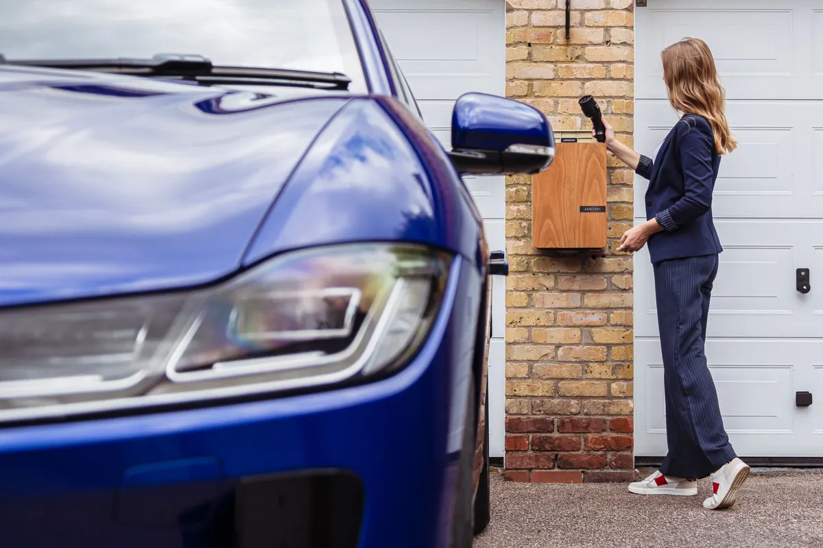 Borne de recharge murale installée devant une maison, voiture électrique branchée